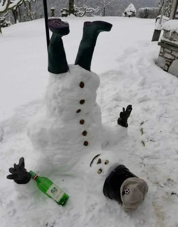 A snowman is depicted lying on its back in the snow, with green rubber boots sticking up from its torso, a green bottle of…