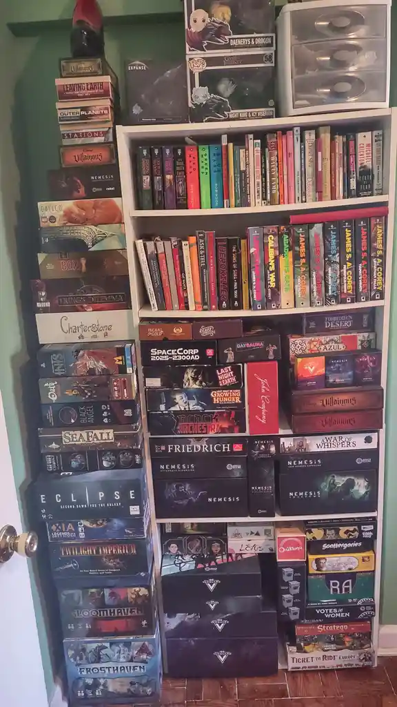 A densely packed white bookshelf and adjacent stack filled with numerous board game boxes and books, showcasing titles like…