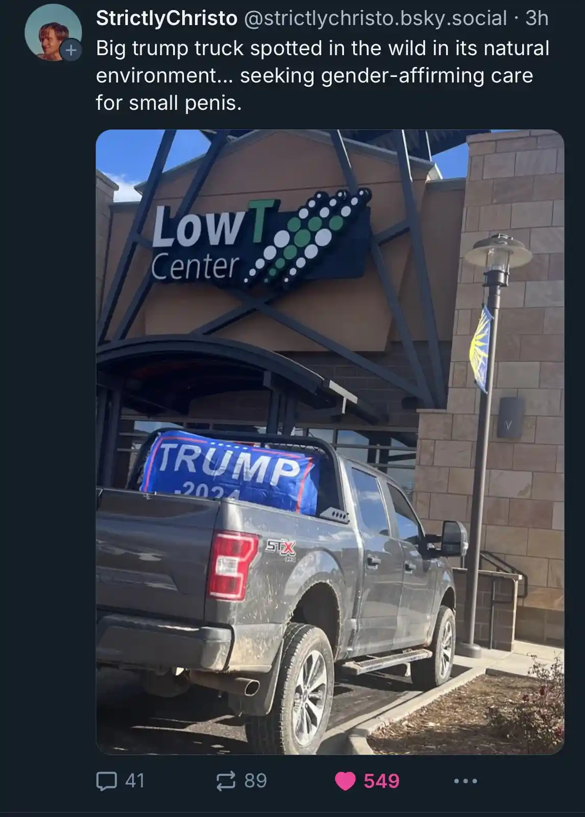 A gray pickup truck with a blue 'TRUMP 2024' banner in its bed is parked in front of a building labeled 'LowT Center'. The…