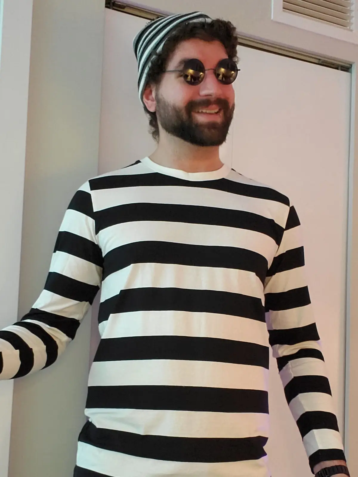 a man with a beard and curly hair wears a black-and-white striped long-sleeve shirt and a matching striped beanie, along…