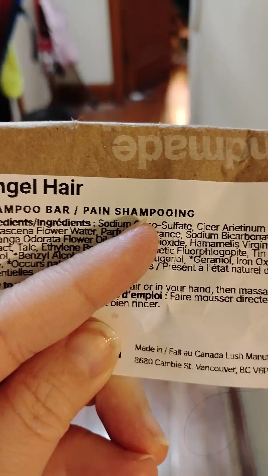 A close-up photo shows a hand holding a cardboard box for a 'Shampoo Bar / Pain Shampooing' product labeled 'Angel Hair'…