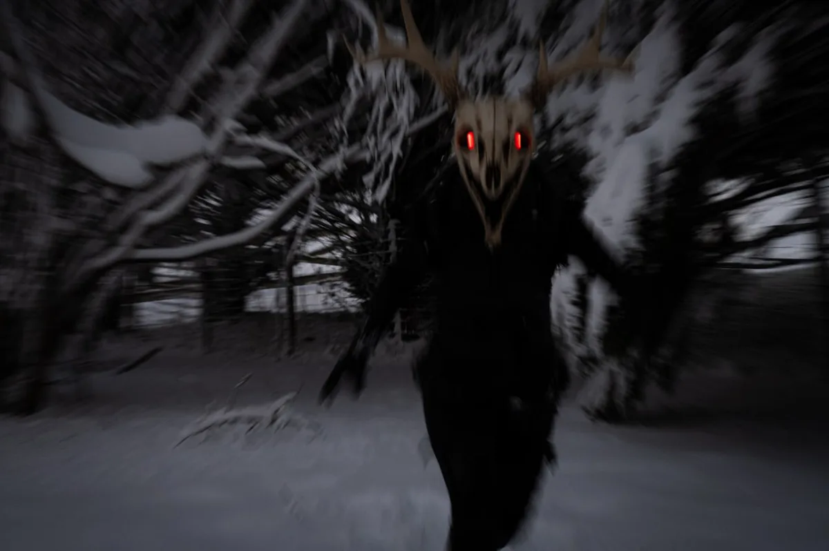 A person wearing a deer skull mask with glowing red eyes and antlers runs toward the camera through a snowy forest, with…