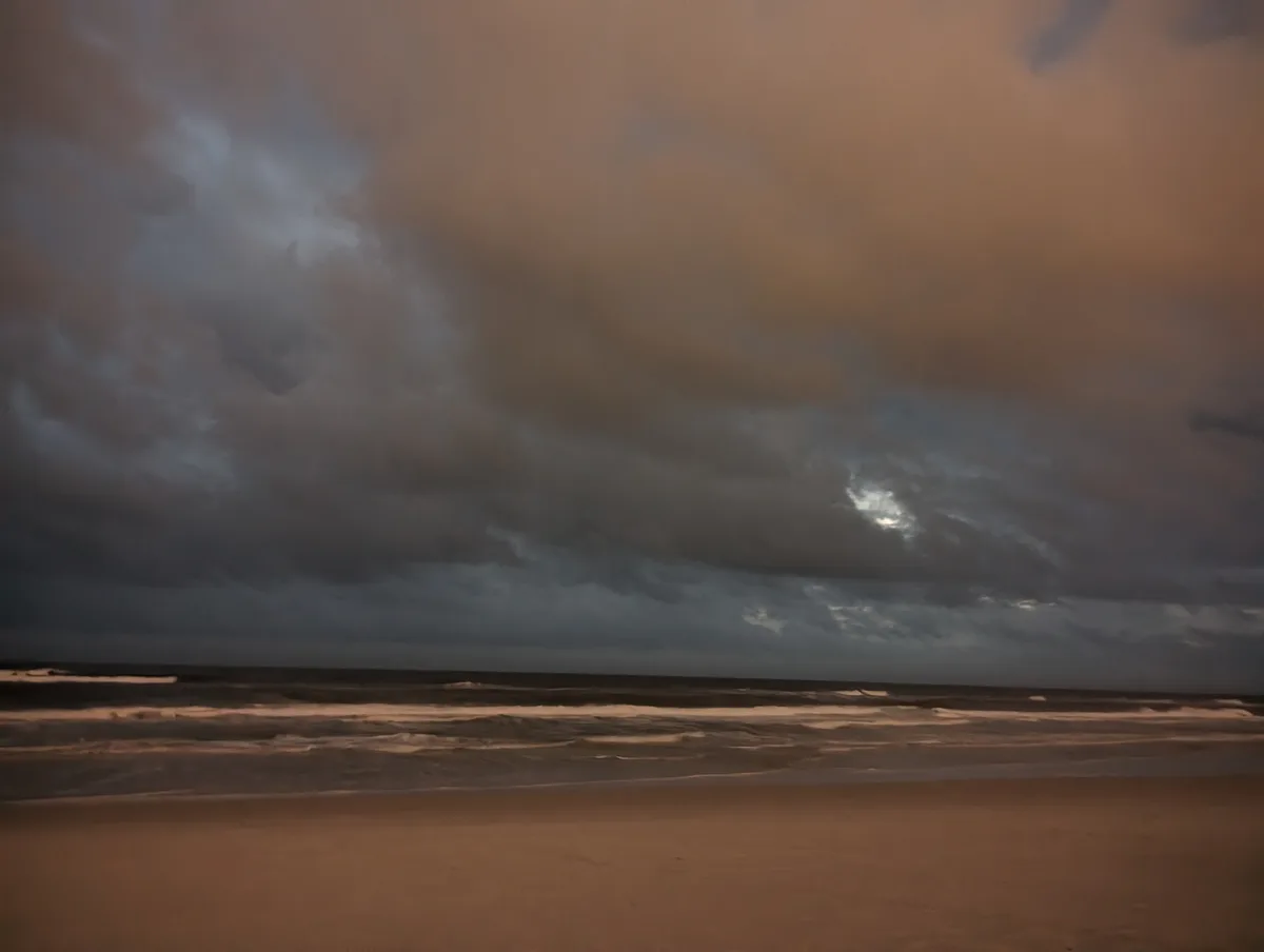 A moody beach scene with dark, dramatic clouds and a dimly lit ocean under a twilight sky. The overlaid text reads 'i'm not…