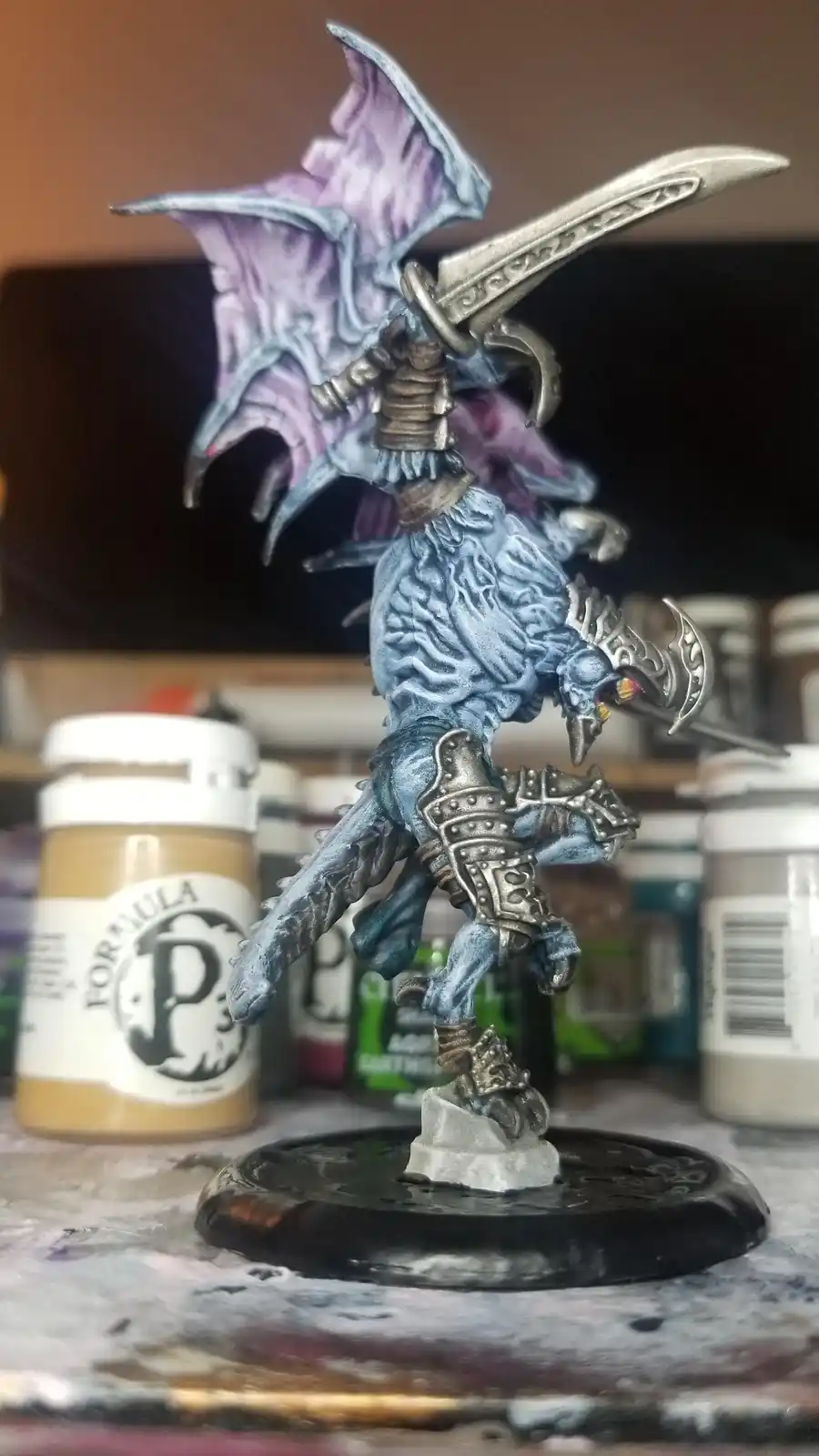 A painted fantasy miniature of a blue-skinned, winged humanoid figure with purple wings, wielding a large sword and a…