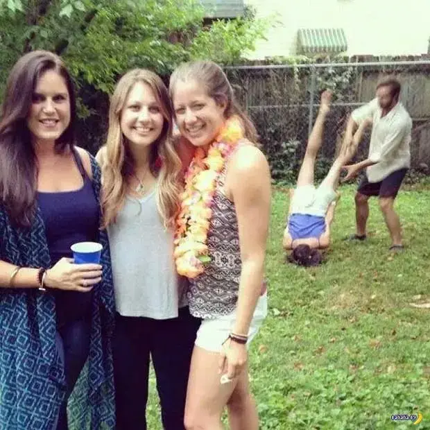 Three smiling women pose for a photo at an outdoor party, with one holding a blue cup. In the background, a man is playfully…