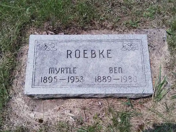 A close-up photo of a gray granite gravestone in grass, engraved with the surname 'ROEBKE' and two names: 'MYRTLE 1895-1953'…