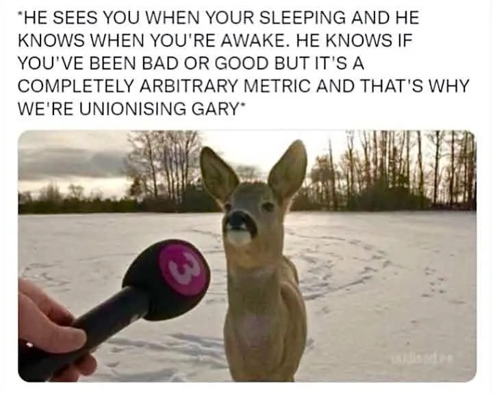 A deer stands in a snowy field, facing a microphone held by a human hand. The microphone has a pink circular logo with the…