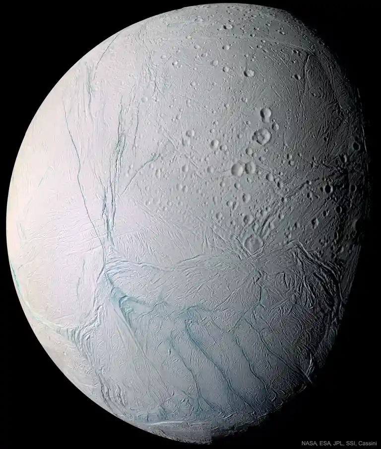 A high-resolution image of Saturn's moon Enceladus, showing its icy surface with prominent cracks, ridges, and impact…