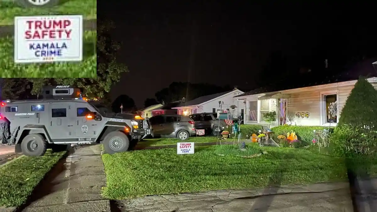 A nighttime photo shows a large armored police vehicle parked in front of a residential house with Halloween decorations. A…