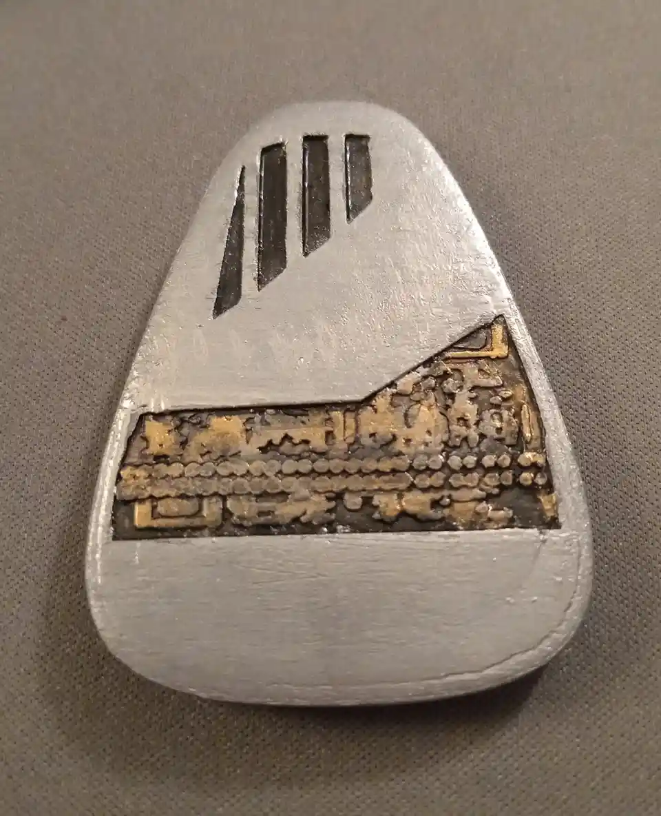 A close-up of a silver-colored, teardrop-shaped object resembling a vintage computer or appliance, featuring three vertical…