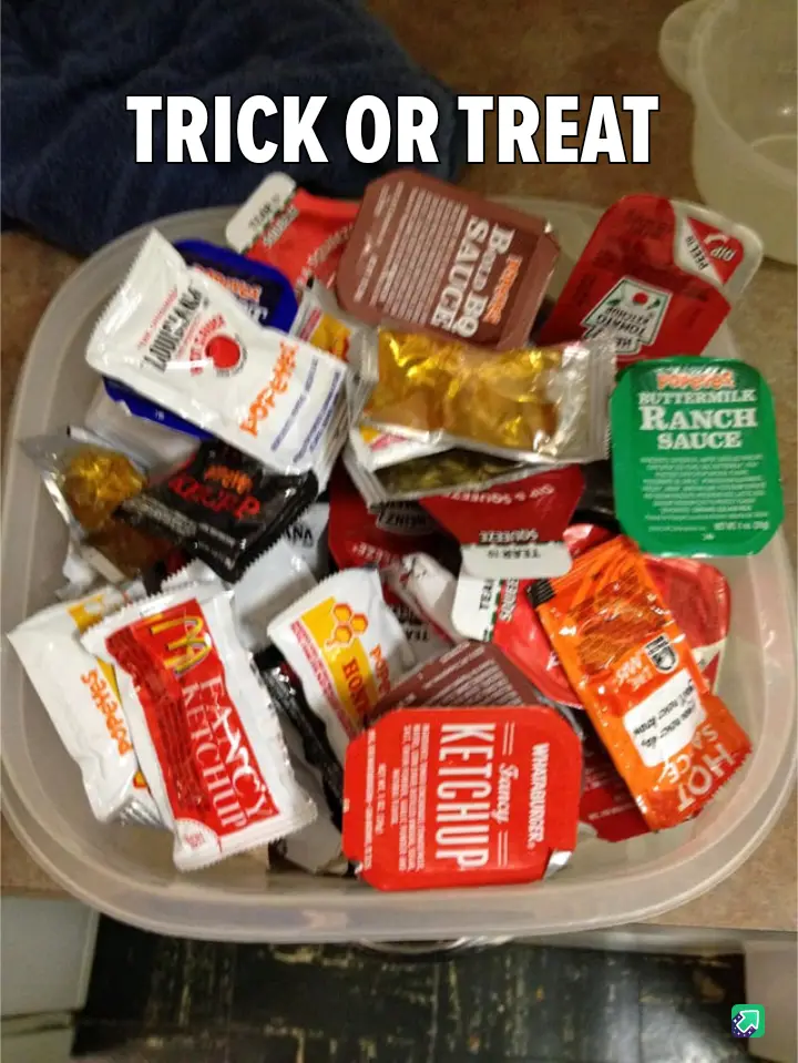 A clear plastic container is overflowing with various fast-food condiment packets, including ketchup, ranch sauce, hot…