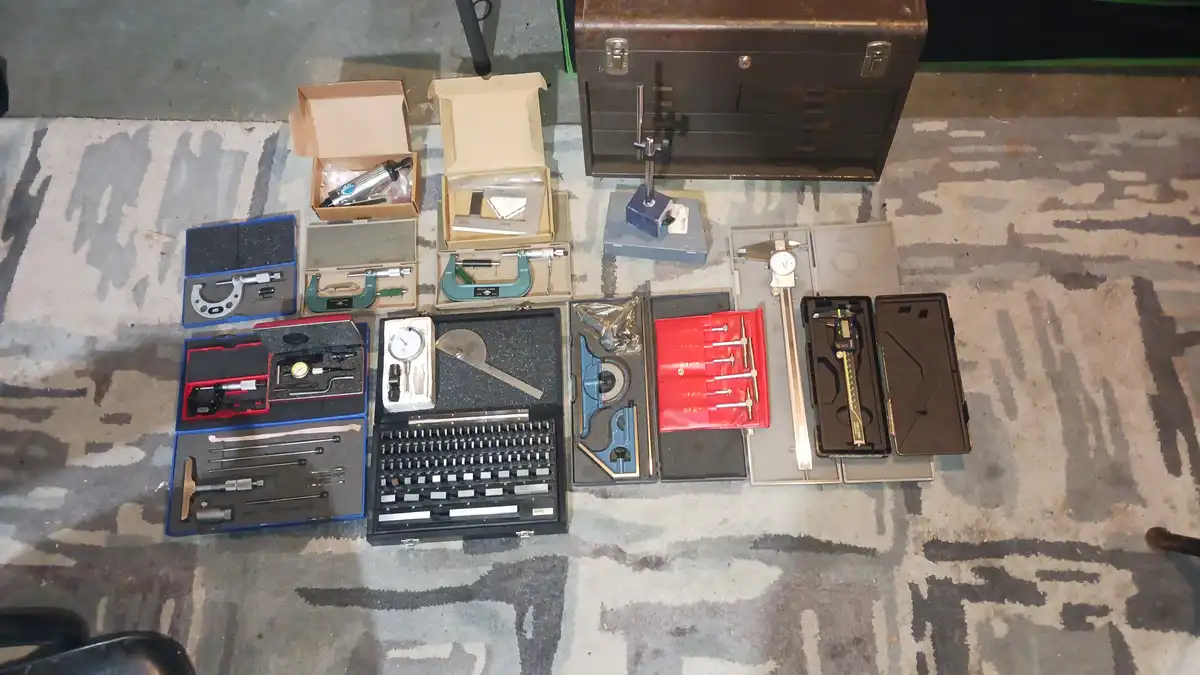 An overhead shot displays numerous precision measuring tools and instruments laid out on a patterned carpet, including…