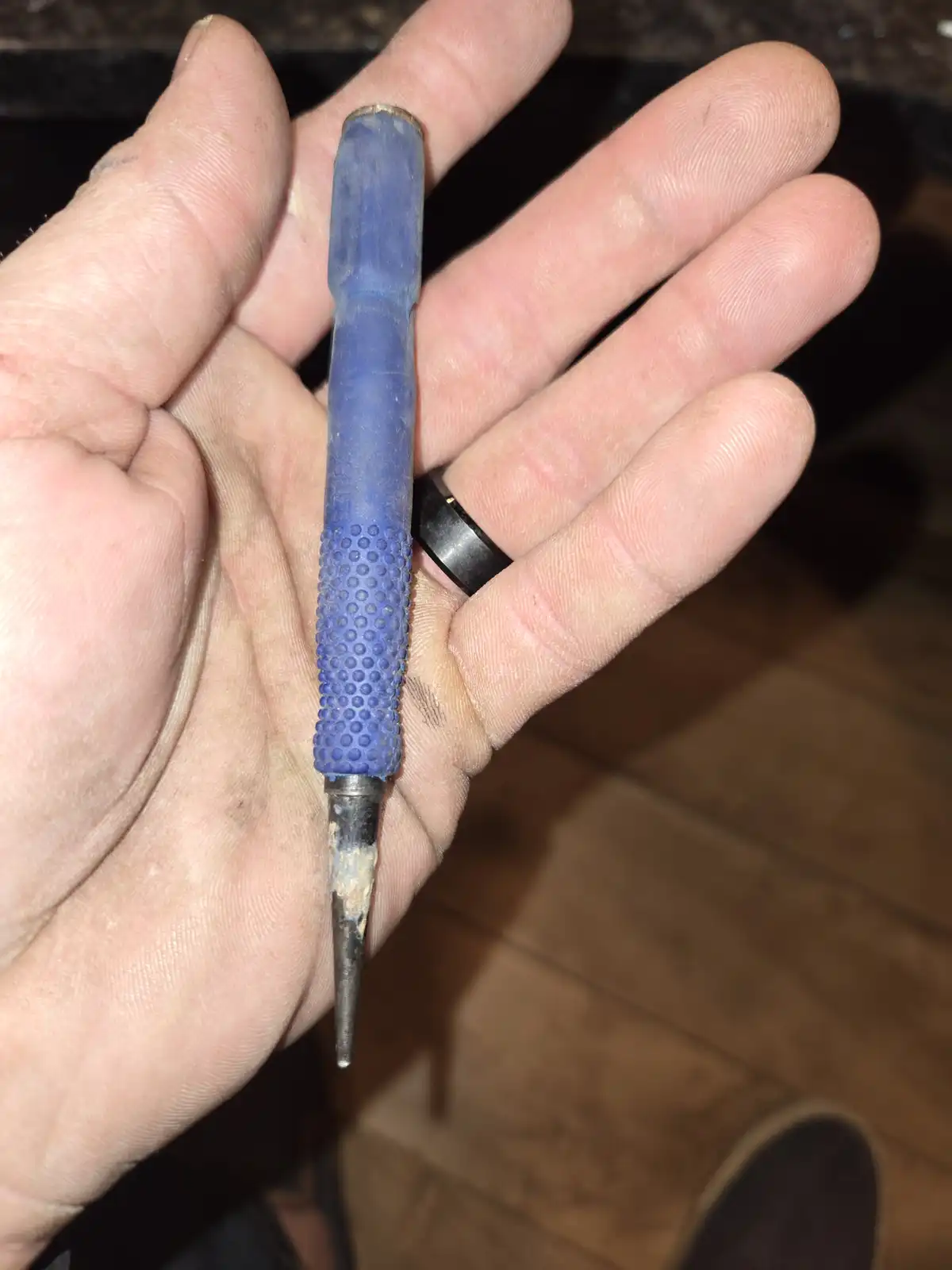 A close-up photo shows a hand holding a blue-handled soldering iron with a visibly worn and dirty tip. The hand has visible…