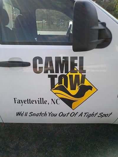 A white tow truck door displays a logo with the text 'CAMEL TOW' above a yellow diamond containing a black camel silhouette…
