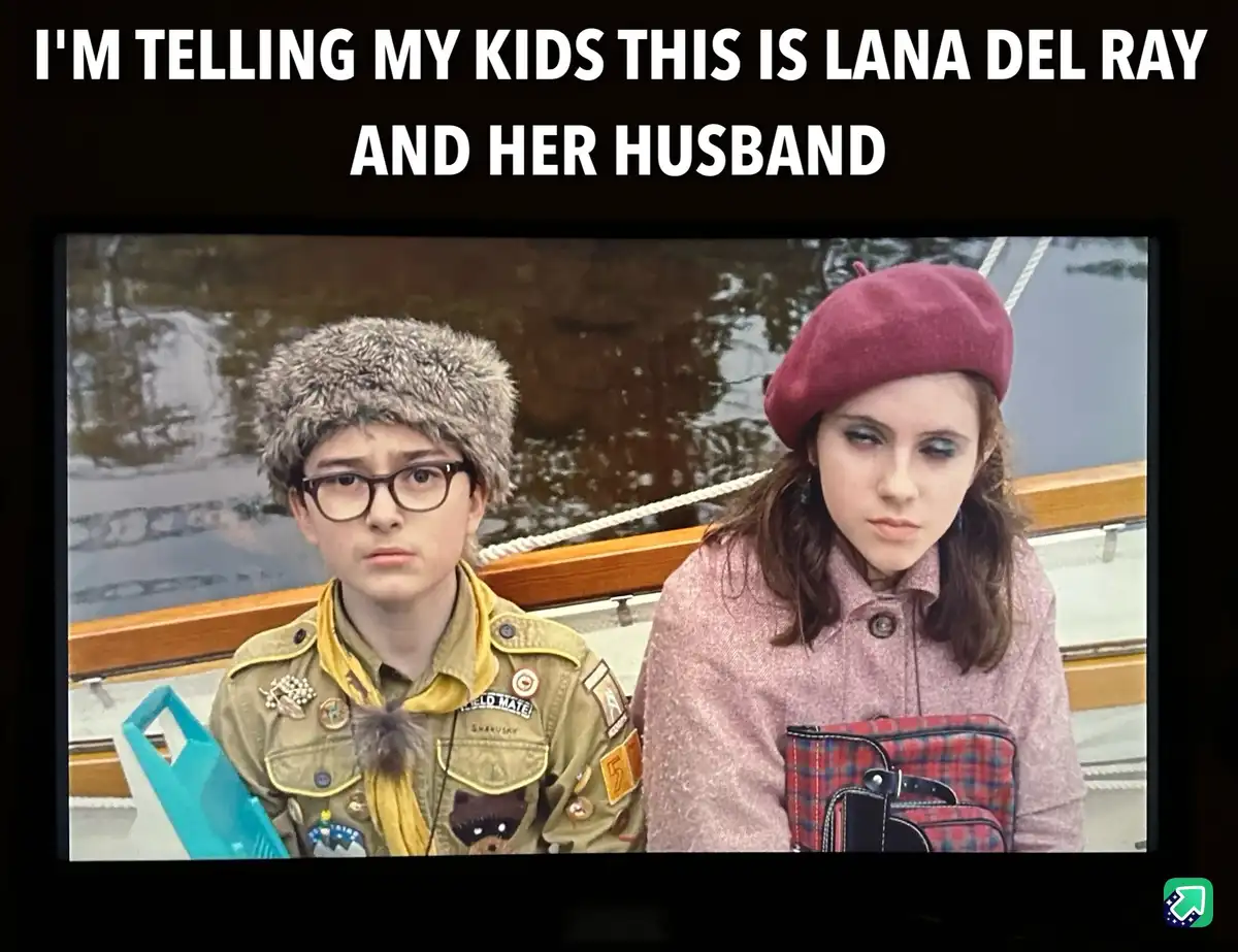 The image shows two young people sitting side by side on a boat, both with serious, unimpressed facial expressions. The…
