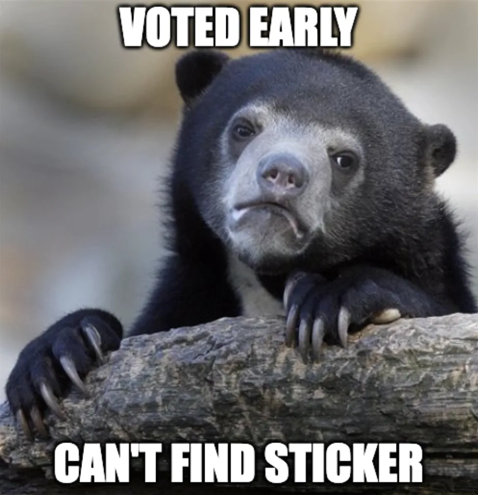 A close-up photo of a black bear with a sad, disappointed expression, resting its paws on a log. The bear has dark fur, a…