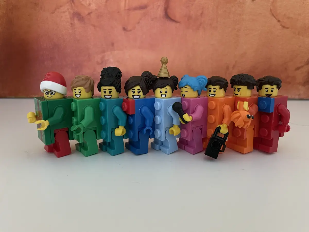 A row of colorful Lego minifigures with varied hairstyles and accessories, including a Santa hat, microphone, boombox, and…