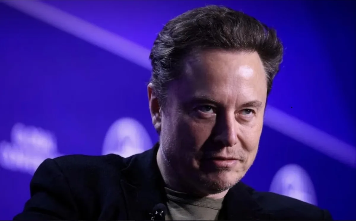 A close-up photo of Elon Musk looking directly at the camera with a serious expression, wearing a dark jacket over a t-shirt…