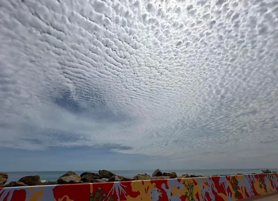 The image shows a vast sky filled with dense, rippling, textured clouds that resemble a giant, white, quilted blanket or a…