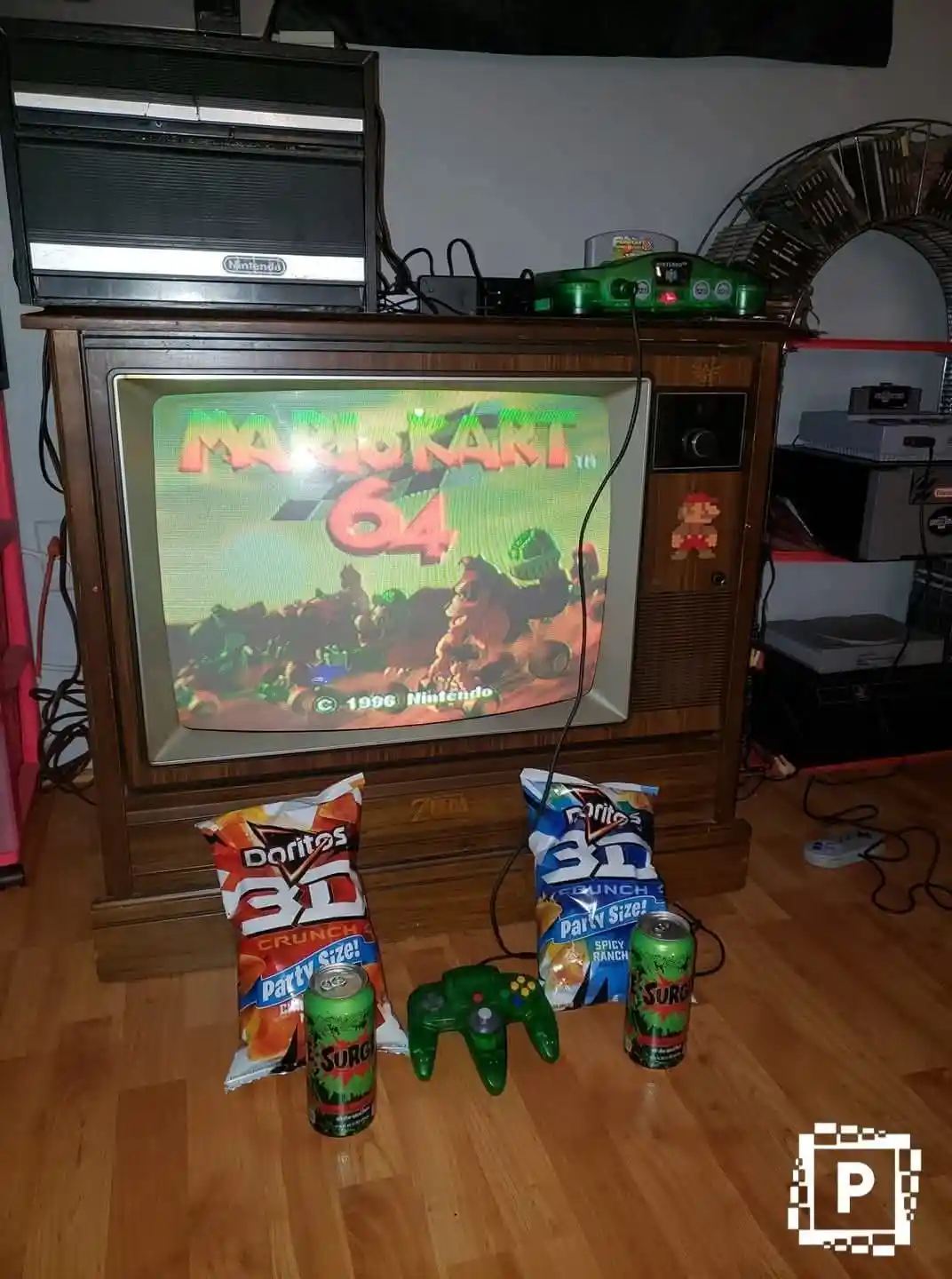 A vintage wooden TV set displays the 'Mario Kart 64' title screen, with a green Nintendo 64 console and controller on top…