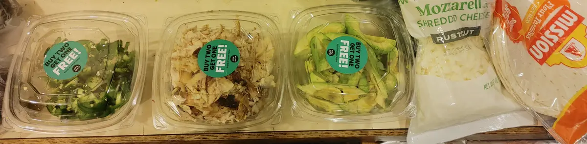 Three clear plastic containers on a shelf hold sliced jalapeños, shredded chicken, and sliced avocado, each with a green…