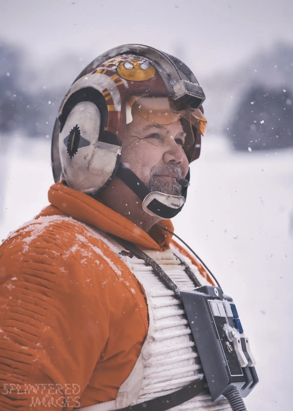 A man dressed in a detailed Star Wars X-wing pilot costume, including an orange flight suit, white armor vest, and a helmet…