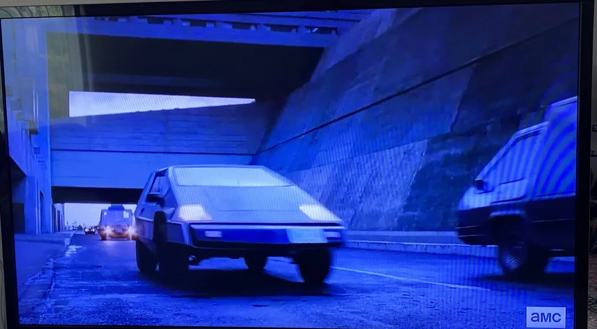 A television screen displays a scene from a movie, showing a futuristic, wedge-shaped car driving through a tunnel under…