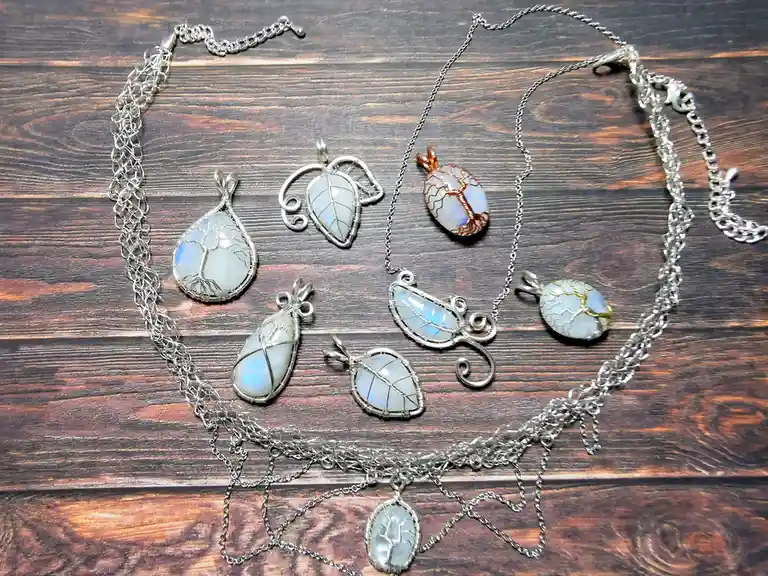 A collection of handmade silver wire-wrapped necklaces and pendants featuring moonstone-like stones with tree of life or…