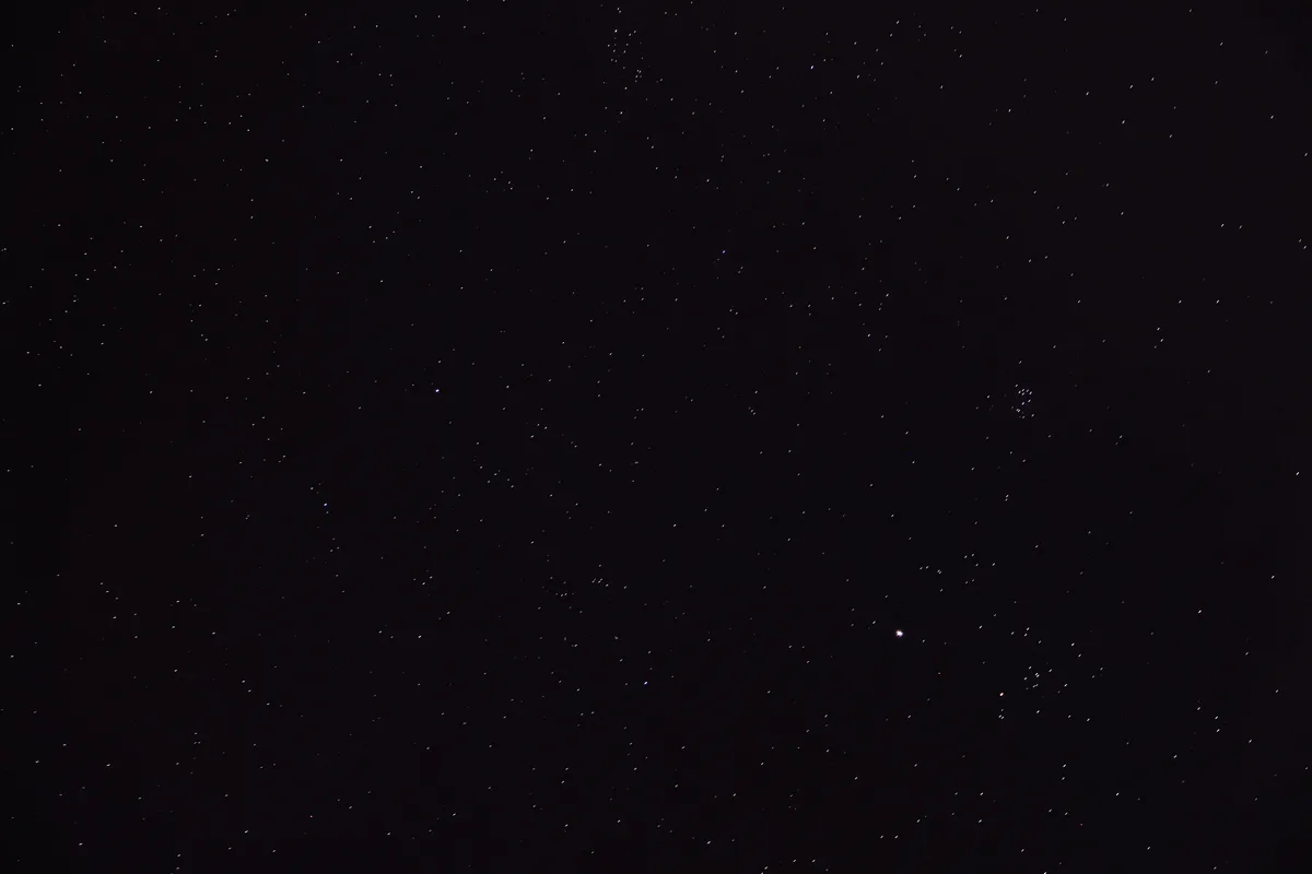 A starry night sky with countless stars scattered across a dark background, featuring a few brighter stars and a faint…