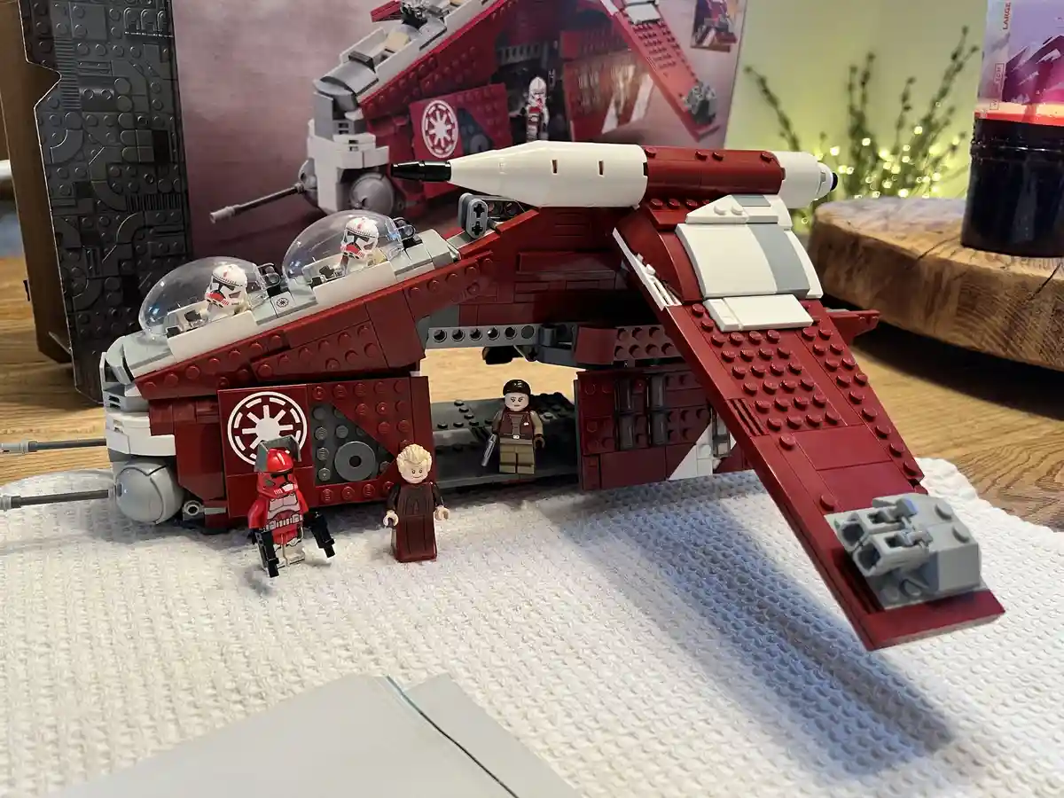 A red and white LEGO Star Wars Imperial shuttle with two pilots in clear domes and several minifigures around it, including…