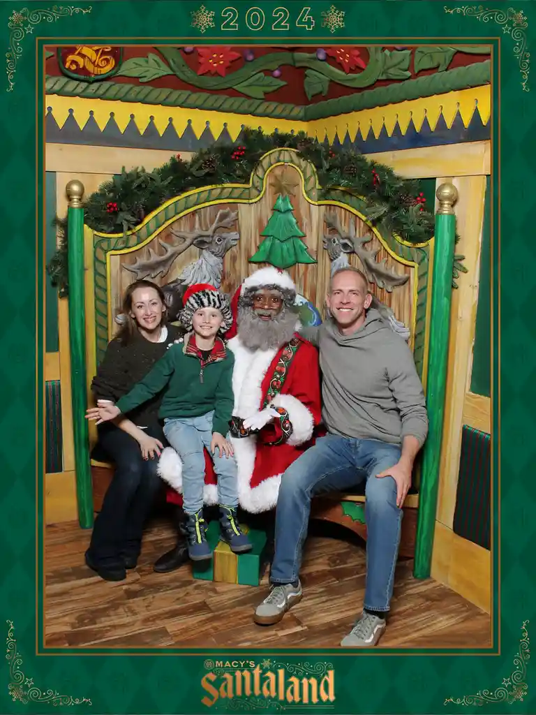 A family photo from Macy's Santaland in 2024 shows a smiling woman, a young boy in a furry hat, and a man posing with a…