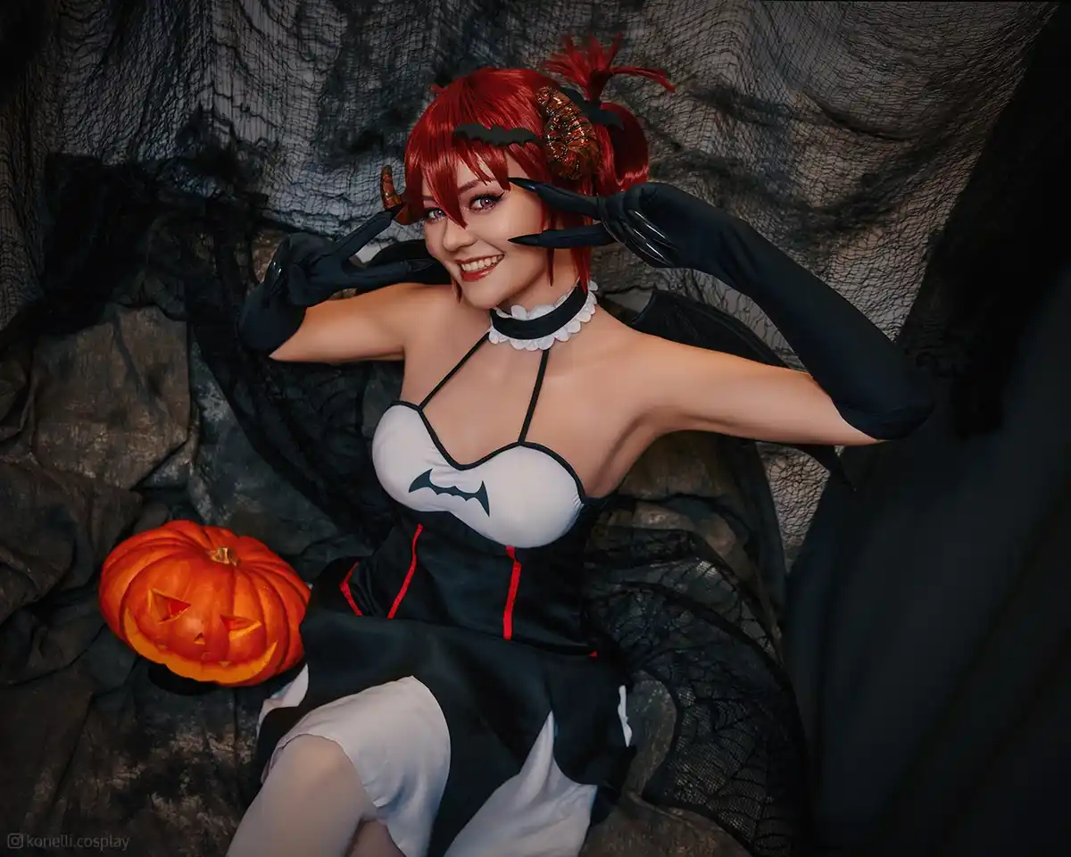A woman with red hair styled in pigtails and wearing a black and white devil-themed costume with bat wings and gloves poses…