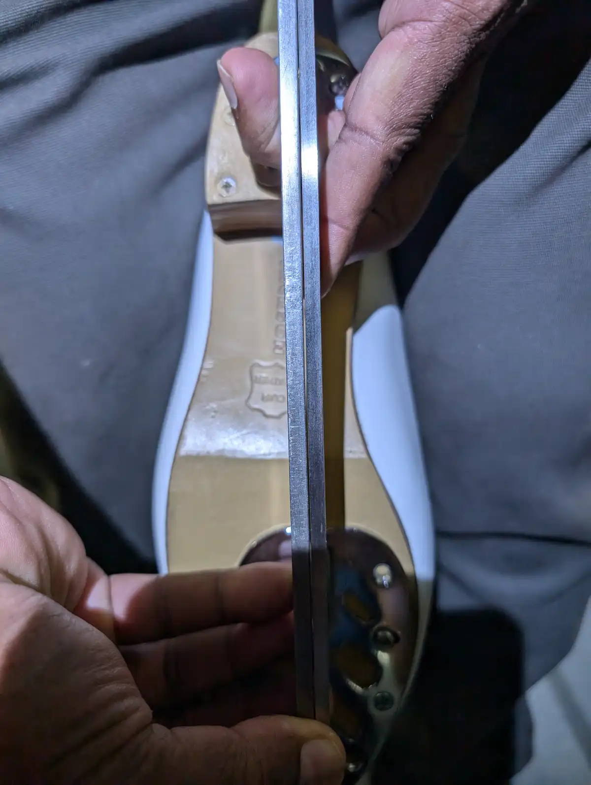 A close-up image shows a person holding a metal ruler vertically against the sole of a shoe, aligning it with the shoe's…
