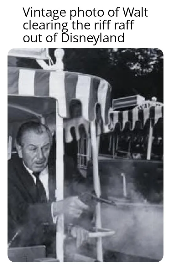 A black-and-white vintage photo shows Walt Disney in a suit, holding a smoking pistol while standing beside a striped canopy…