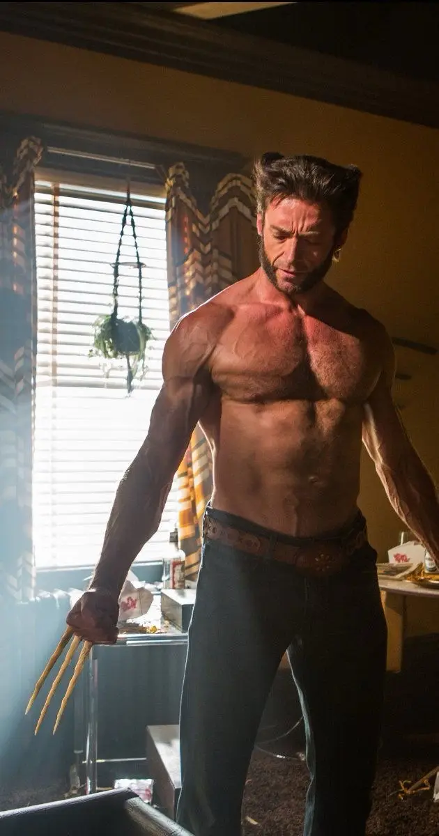 A shirtless, muscular man with pointed ears and claws extended from his knuckles stands in a dimly lit room with a window…