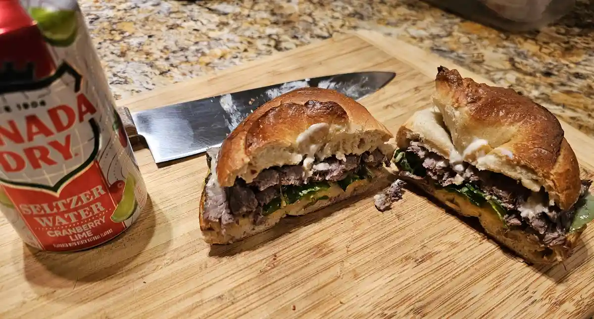 A freshly made sandwich, cut in half and resting on a wooden cutting board, reveals layers of meat, greens, and sauce…