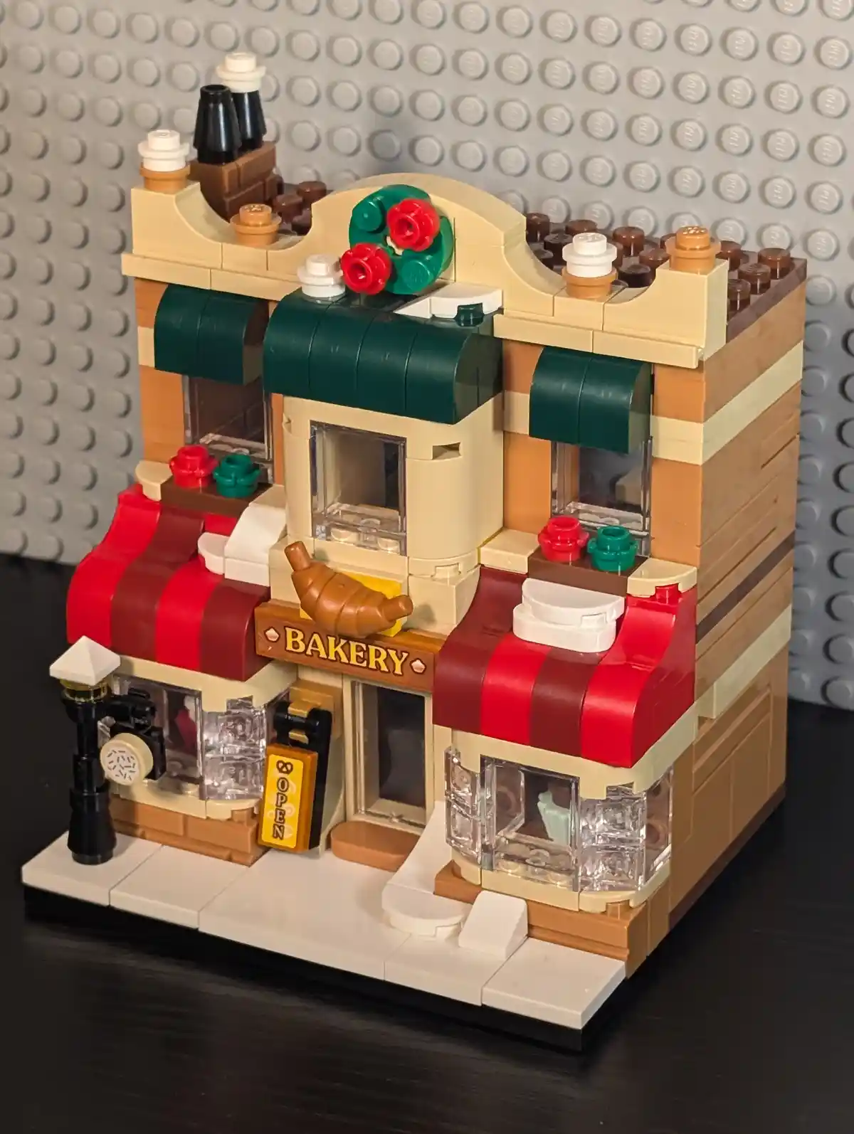 A detailed LEGO model of a two-story bakery with red striped awnings, a sign reading 'BAKERY', and a croissant decoration…