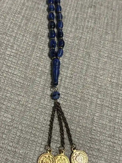 A close-up photo shows a string of blue beads with a decorative blue bead and three dangling gold-colored coin charms…