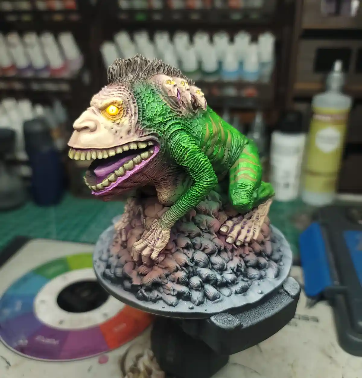 A highly detailed, painted miniature monster with green scaly skin, a large main head with a yellow glowing eye, and three…