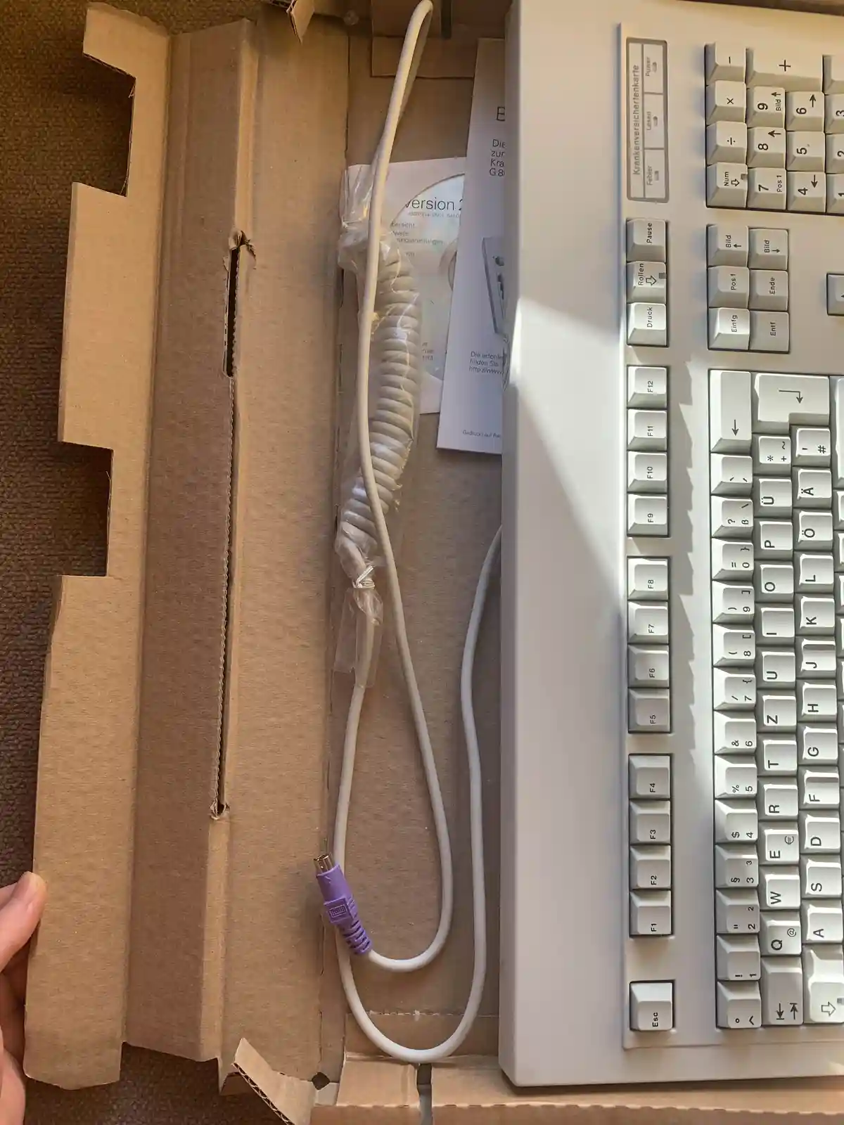 A white computer keyboard with German labels like 'Krankenversichertenkarte', 'Pause', and 'Druck' sits next to a coiled…