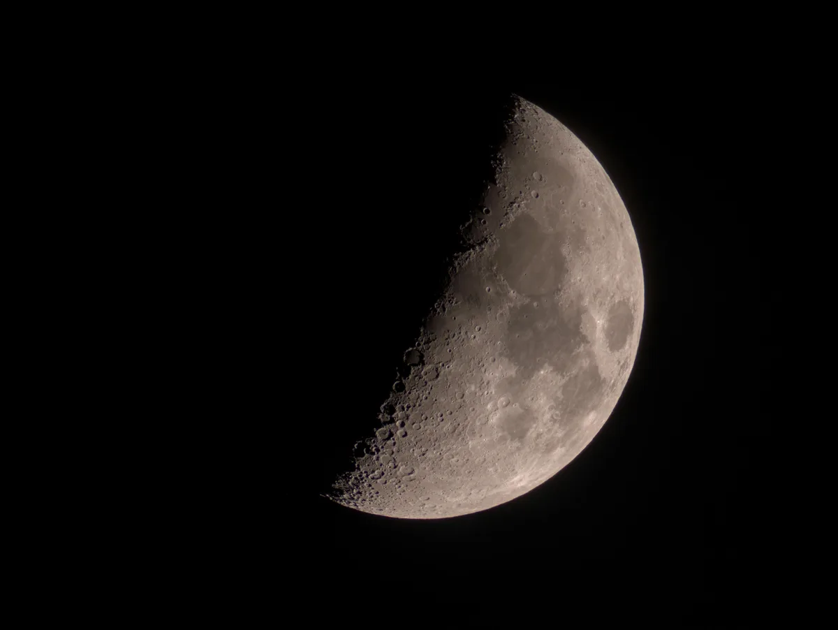 A high-resolution photograph shows a crescent moon against a black sky, its cratered surface visible on the illuminated…