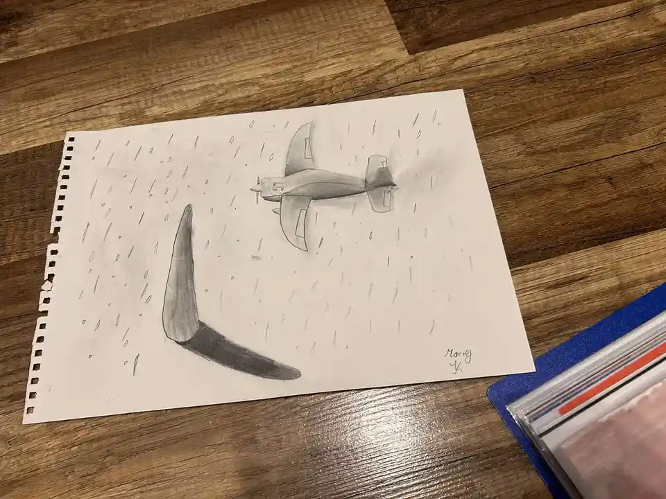 A pencil drawing on a sheet of paper shows a small airplane flying through rain, positioned directly above a large, shaded…