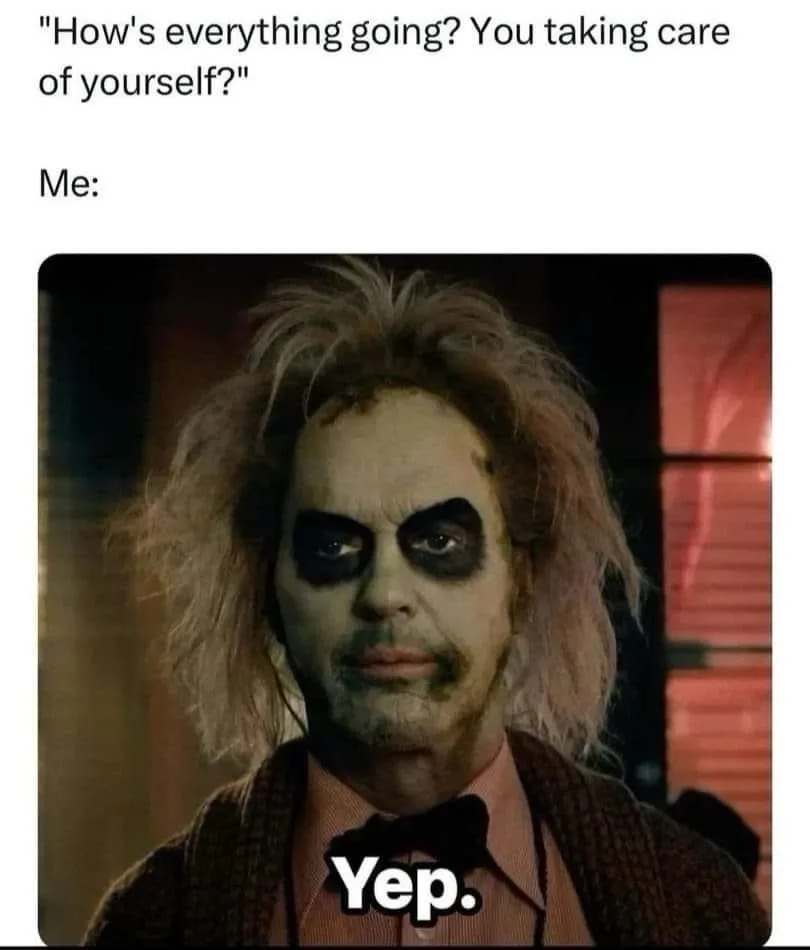 The image shows a close-up of the character Beetlejuice with messy hair, pale makeup, and dark eye makeup, wearing a brown…