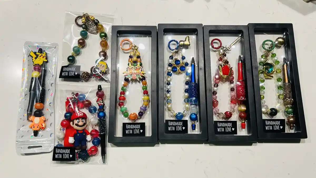 Several colorful, beaded keychains and pens, some featuring Nintendo characters like Pikachu, Mario, and Zelda, are…