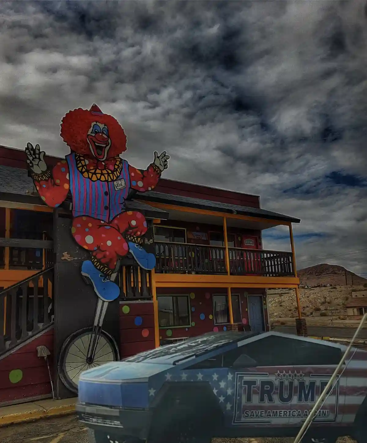 A large, colorful clown cutout mounted on the side of a two-story building under a dark, stormy sky. In the foreground, a…