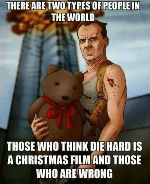 A bloodied, muscular man with a stern expression holds a brown teddy bear with a red bow, standing in front of a burning…