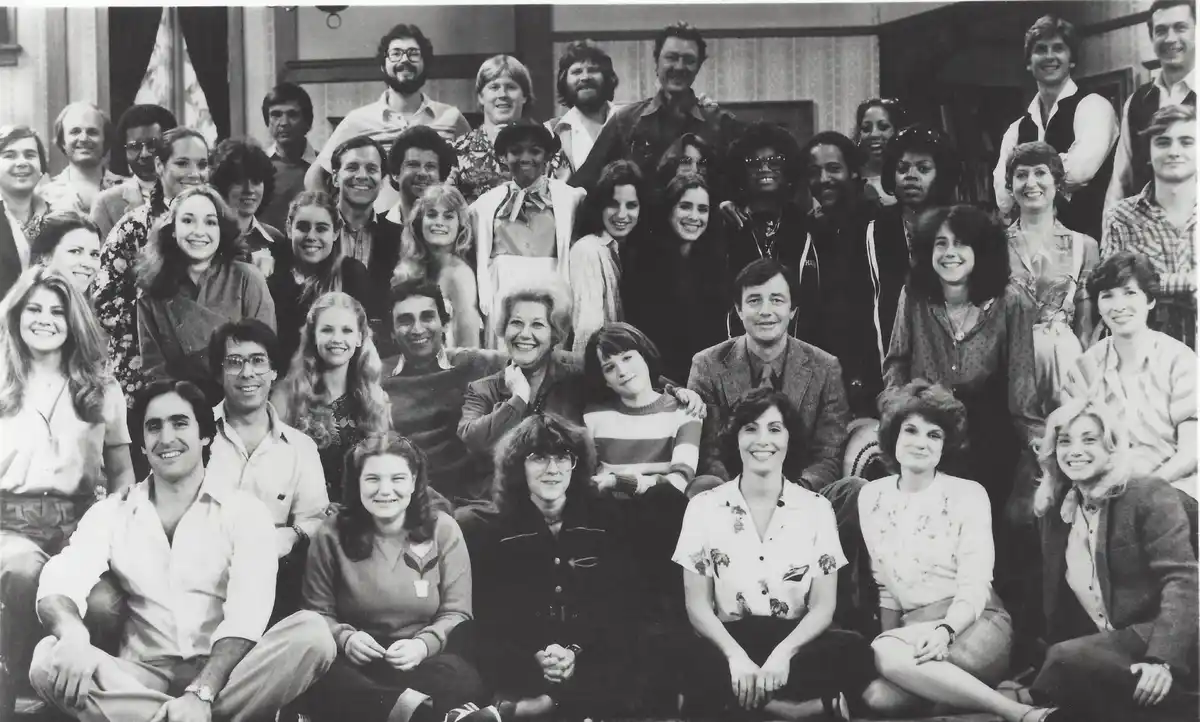 A black-and-white group photo of the cast of the 1970s TV show 'The Love Boat,' smiling and posing in rows. The overlaid…