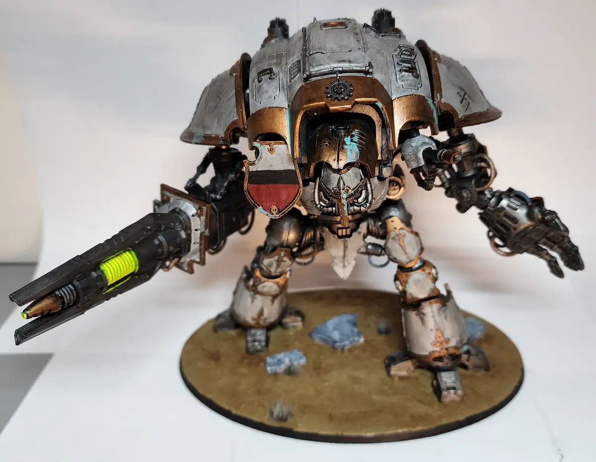 A heavily armored, bipedal war machine model with a large cannon arm and a shield bearing a red and black emblem stands on a…