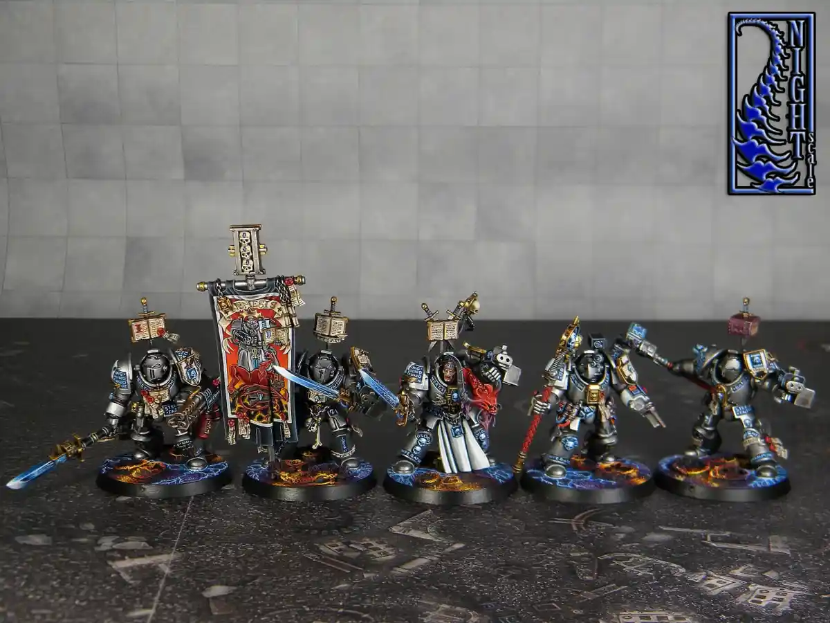 Five intricately painted miniature warhammer 40k space marines stand in a line on a dark, textured surface against a gray…