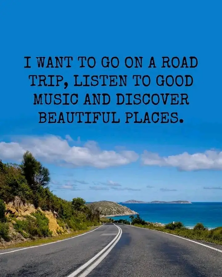 A scenic coastal road stretches into the distance under a bright blue sky with scattered clouds, flanked by green vegetation…